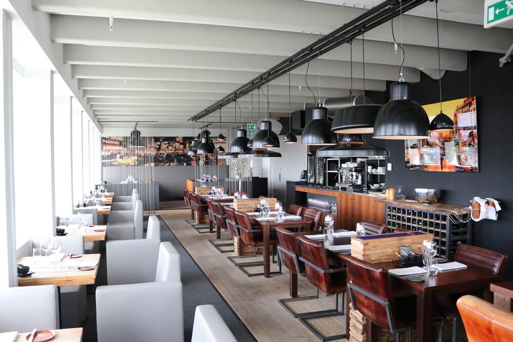 A modern style restaurant, with black penant lights from the ceiling and wood and leather features for the tables and chairs. 