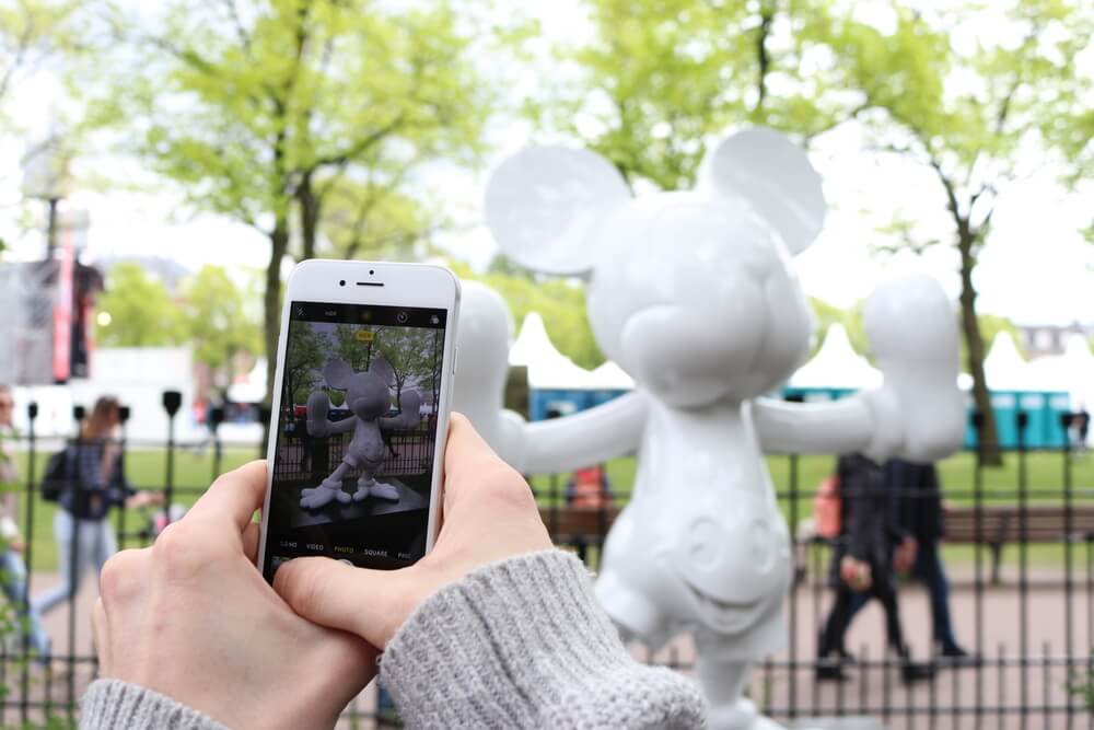 A white iPhone, taking a photo of a white Mickey Mouse statue
