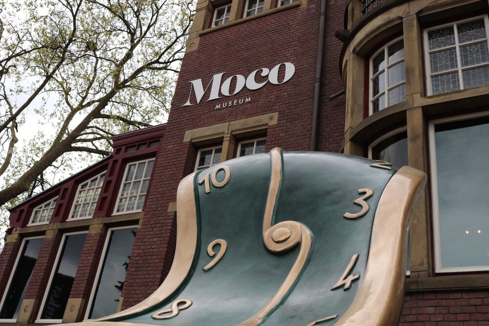 The exterior of the Moco Museum in Amsterdam, featuring a large melting clock in Dali style. 