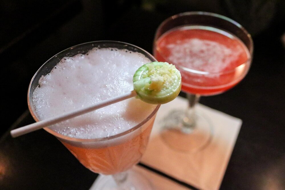Two cocktails, shown from above. One with a green lollipop resting on top. 