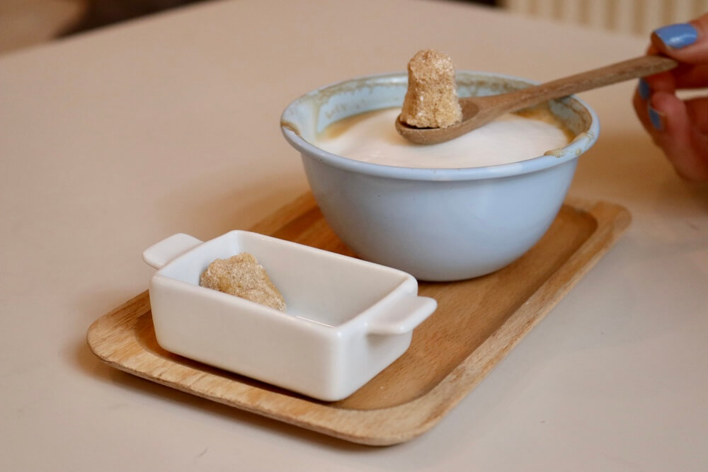 A small blue bowl of frothy milk and small dish of brown sugar cubes