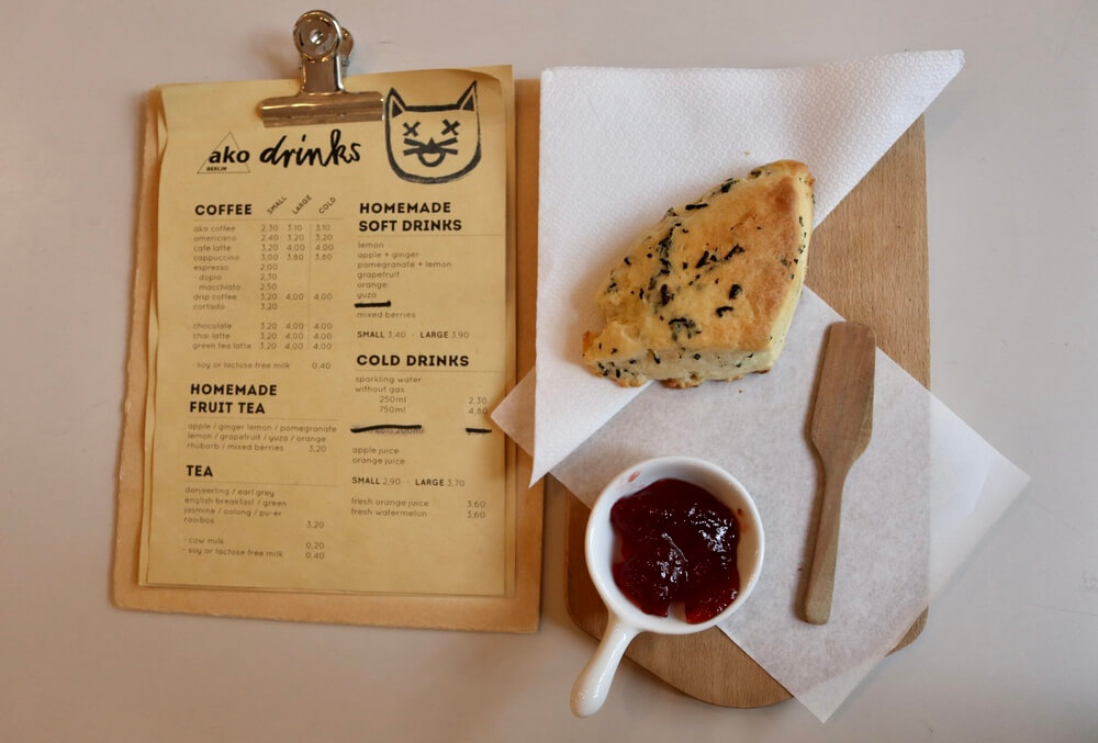 A menu on a wooden clip board on the left and to the right a large scone with small ramekin of strawberry jam