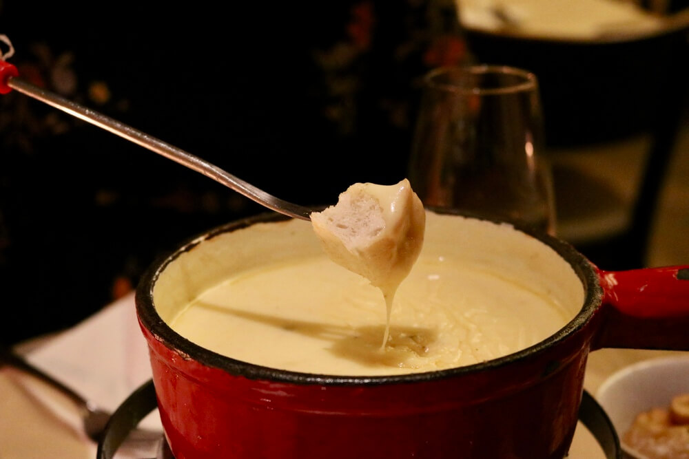 A red fondue pot with bread covered in cheese sauce
