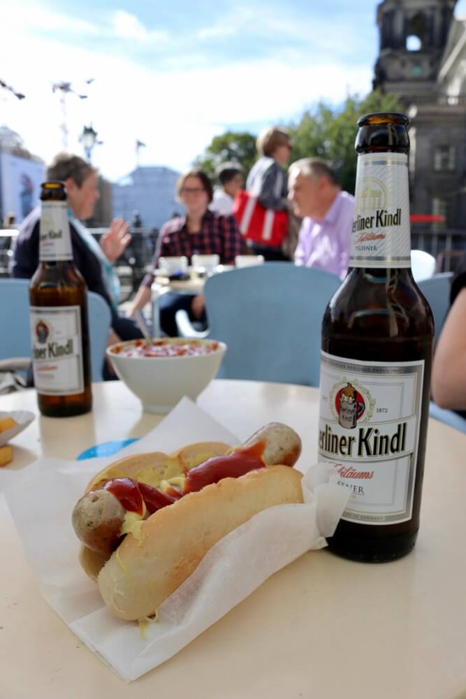 A bottle of beer with a hot dog with ketchup and mustard