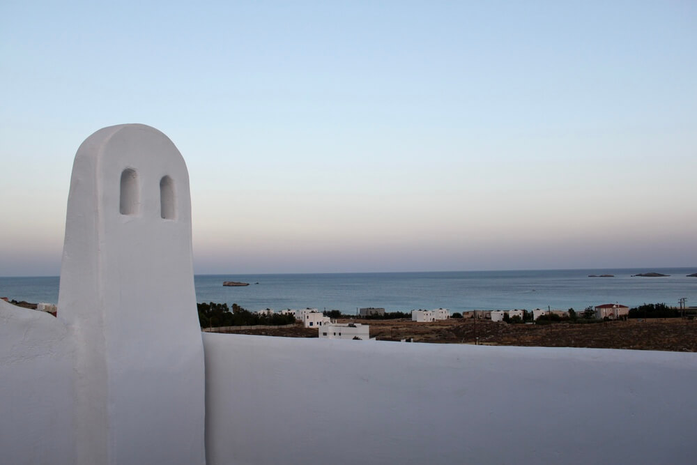 A white stone wall in front of a blue bay at sunset