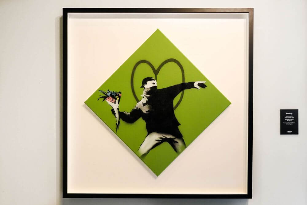 Banksy piece showing a green square on its point with a masked man throwing a bunch of flowers