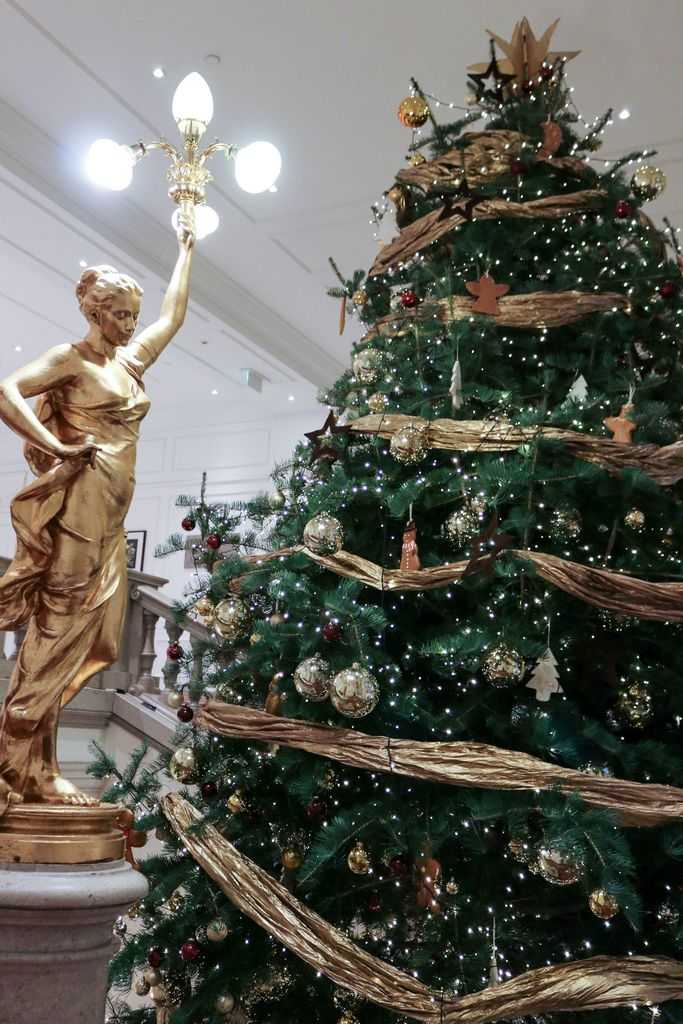 Corinthia Budapest - Christmas tree with gold ribbon next to a golden lady statue